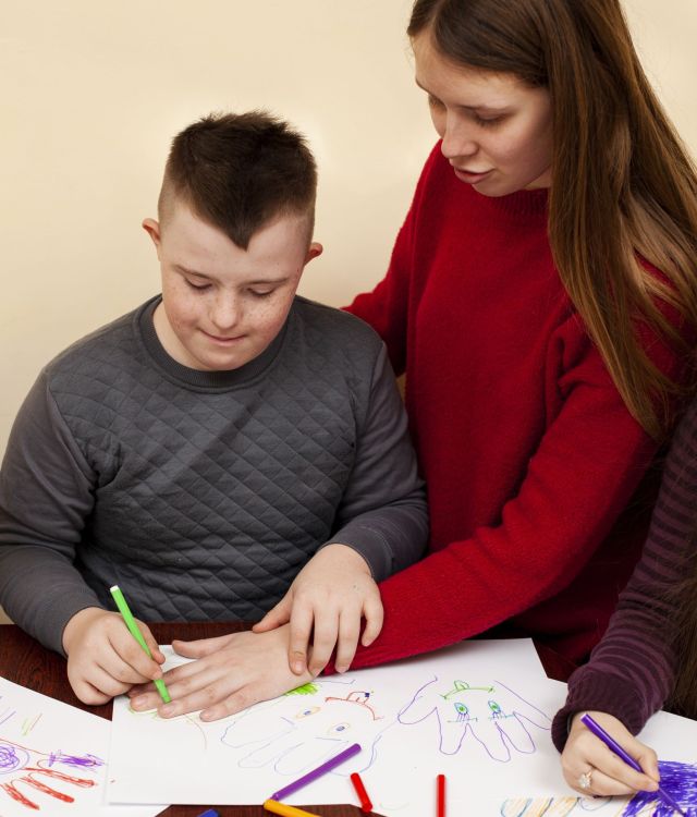 woman-helping-boy-with-down-syndrome-draw